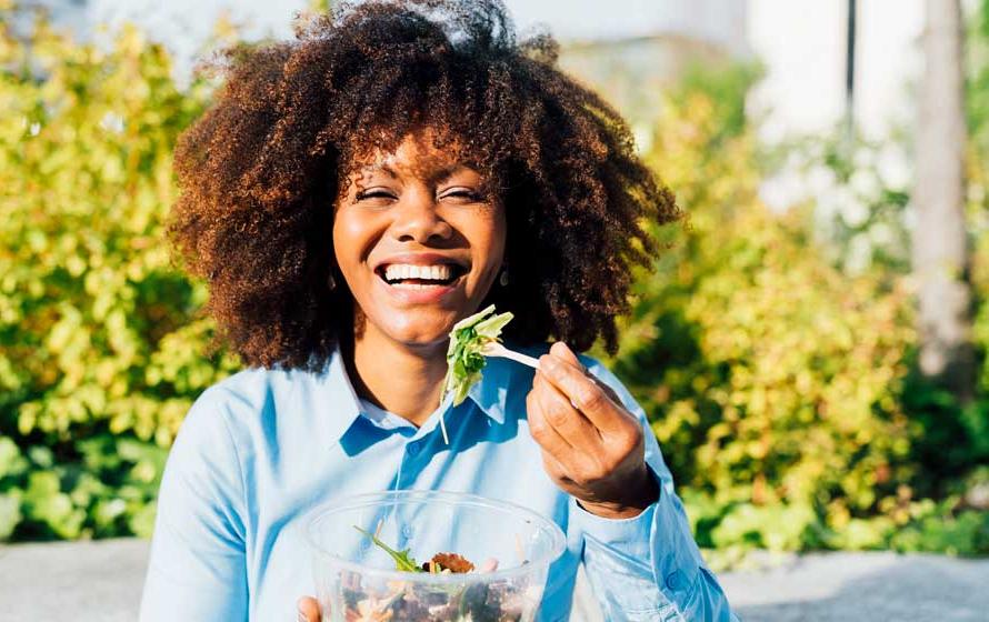 Happy businesswoman eating salad on sunny day