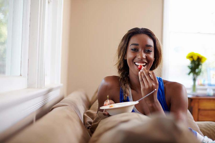 Young woman sitting on couch, eating and smiling