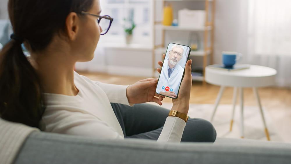 Woman sitting on couch at home using telehealth service on her phone